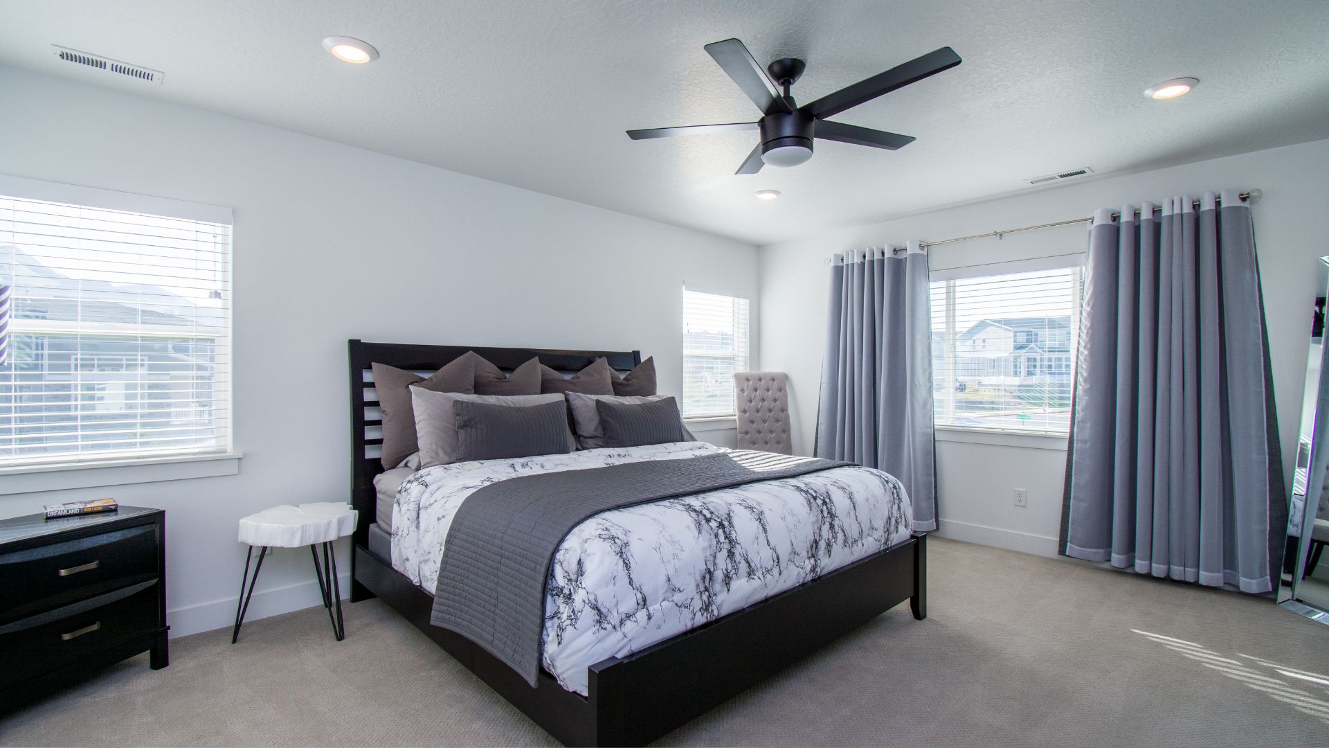 Modern bedroom with marble bedding, gray curtains, and ceiling fan