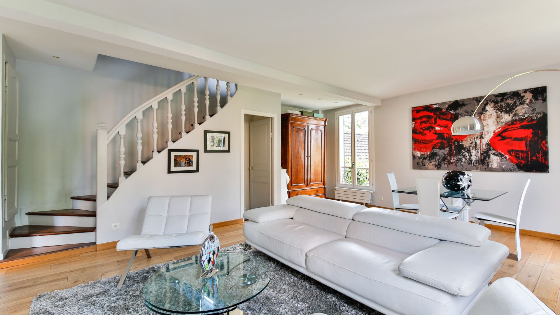 Modern living room with white sofa, wooden stairs, and red abstract art