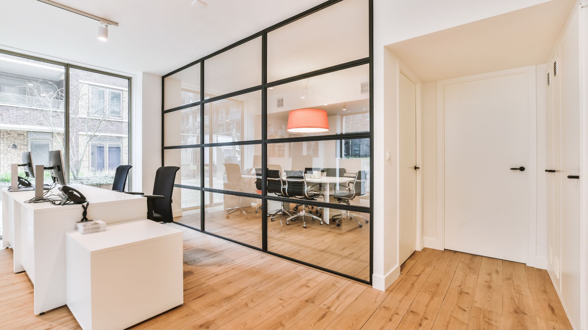 Modern office with glass partition, white desks, and wooden floor