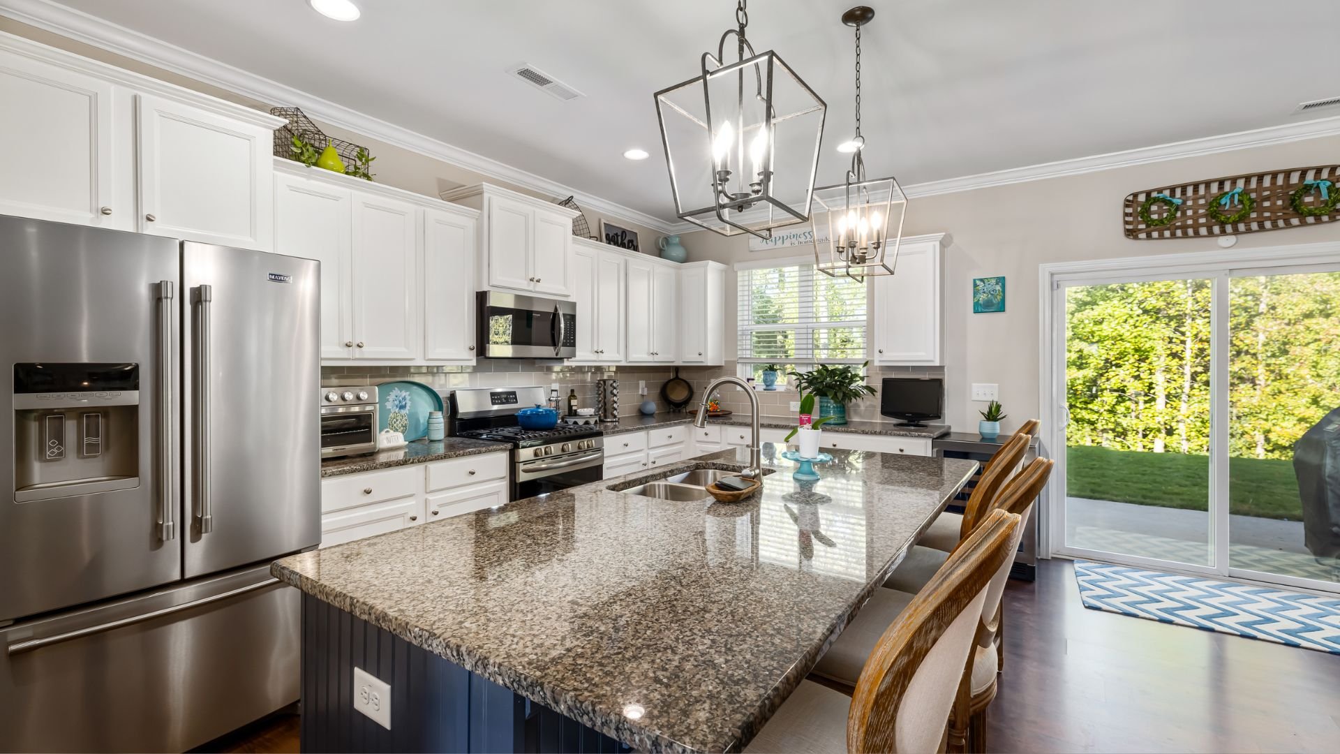 Modern white kitchen with granite island, stainless steel appliances, and garden view