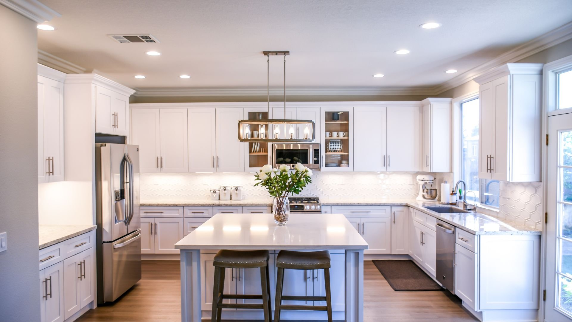 Modern white kitchen with island, stainless steel appliances, and hanging light fixture
